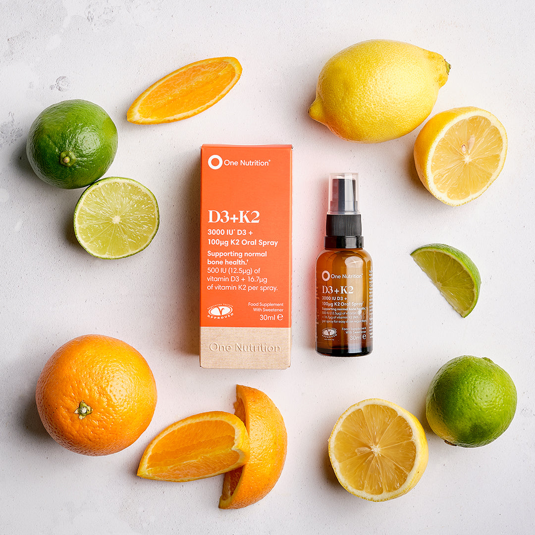 One Nutrition D3+K2 supplement bottle and box surrounded by citrus fruits on a light background
