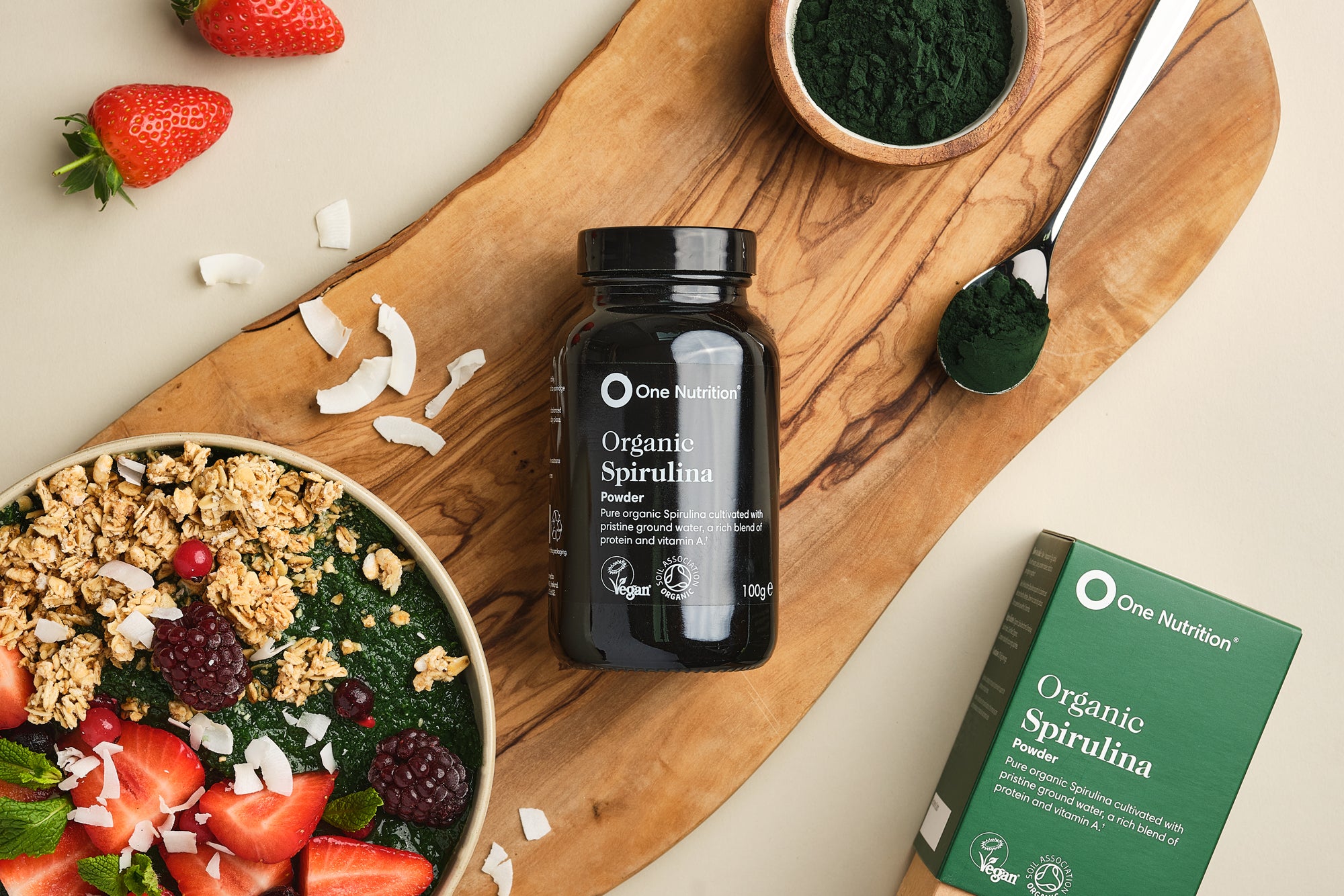 One Nutrition Organic Spirulina powder bottle and packaging on a wooden board with a bowl of salad and strawberries.